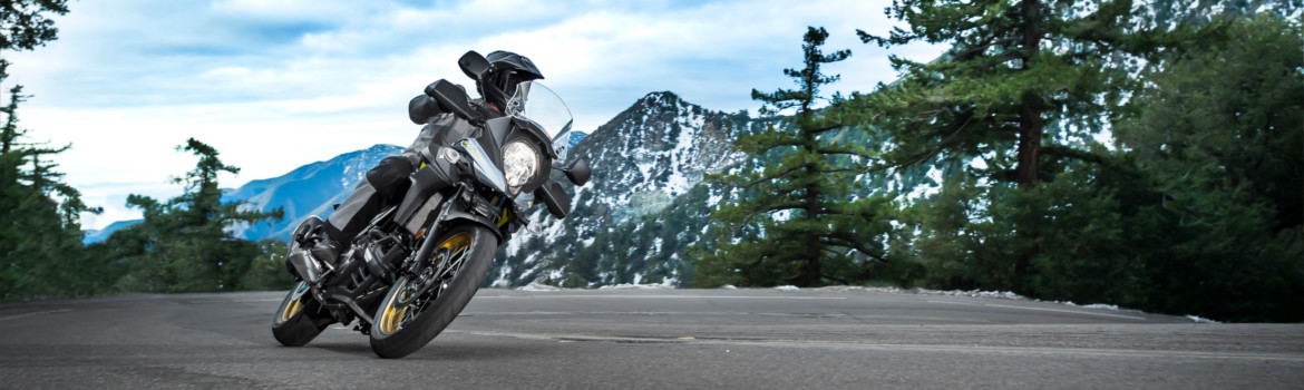 Rider on a Suzuki  V-STROM 650XT taking a turn on a highway road with mountains and trees in the background